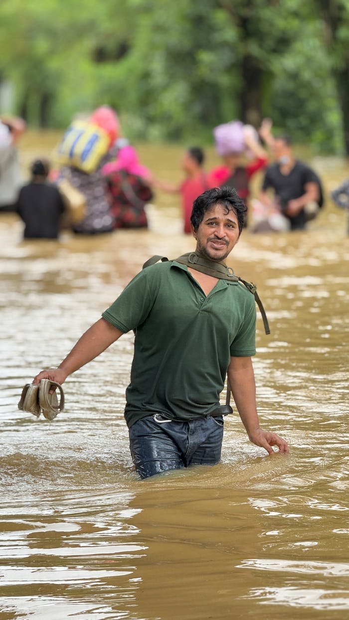 about-01 Man wades through floodwaters holding shoes as people struggle behind. Resilience in disaster.