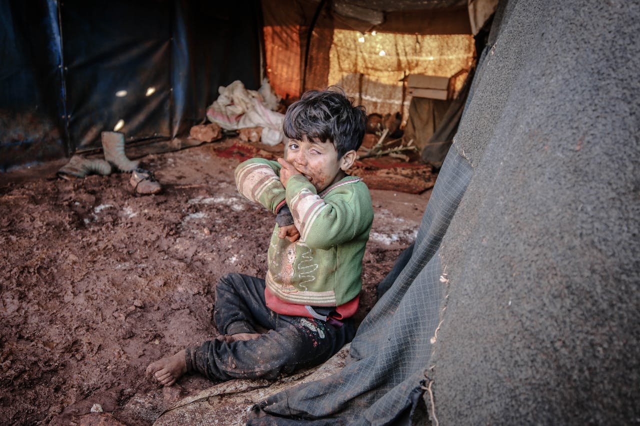 hero-contact A young child with a dirty face sits in a refugee camp tent in Idlib, Syria.